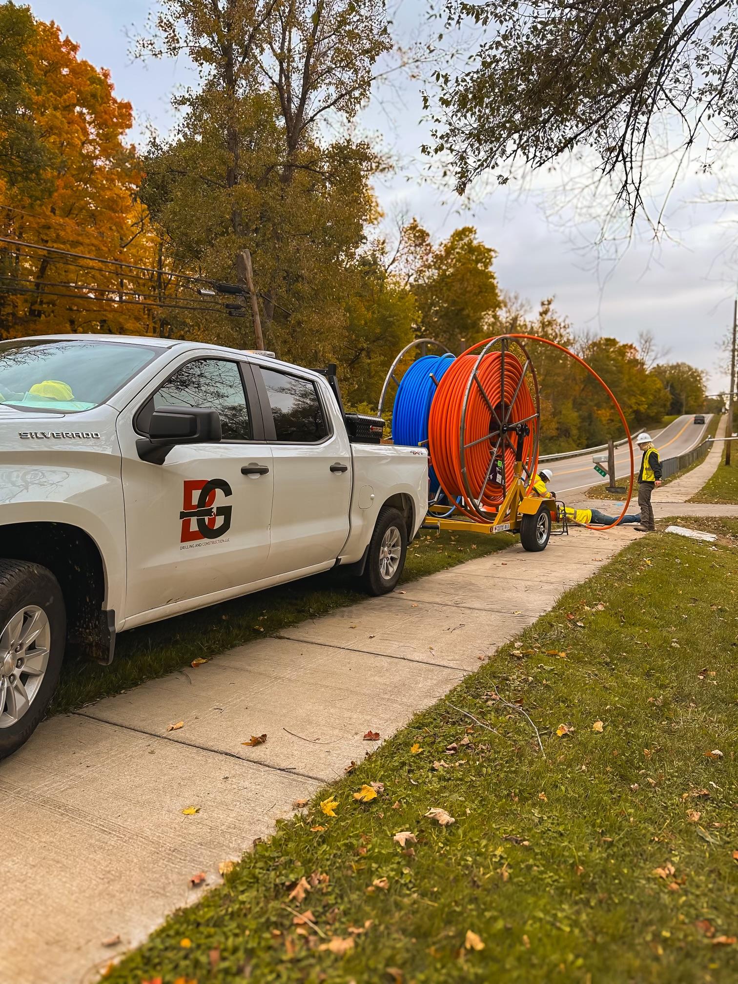 B&G Drilling & Construction truck towing a fiber conduit reel on a job site